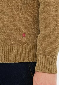 Maglione brown in maglia con un motivo testurizzato, polsini a coste e un piccolo etichetta rossa vicino all'orlo, che evidenzia il suo design casual.