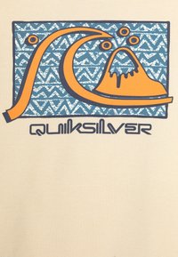 Un tejido de color crema presenta un fondo de estampado azul y blanco con un gráfico de olas y montañas en naranja. El texto dice "Quiksilver" en negro.