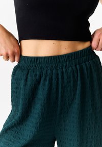 Dark green textured pants with an elastic waistband, paired with a black cropped top, focusing on the waist and fabric details.