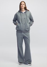 Grijze sweatshirt met capuchon, voorrits en knopen; gecombineerd met bijpassende wijde broek; gemaakt van zachte stof; casual stijl.