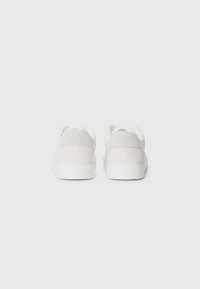 Valkoiset tennarit, joissa on sileä ja karheaa mokkaa oleva päällinen, litteä kumipohja ja ei näkyvää brändäystä. Yksinkertainen, minimalistinen muotoilu.