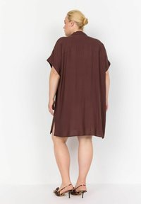 Abito corto marrone, setoso, con colletto, maniche corte e spacchi ai lati. La vista dal retro mostra un design fluido e liscio con una vestibilità morbida.