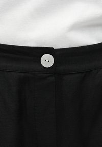 Λευκό κουμπί στερεώνει μαύρη ζώνη σε μαύρο ύφασμα, κάτω από ένα λευκό υφασμάτινο φόντο.