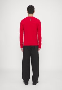 Maglietta rossa a maniche lunghe con scollatura a girocollo, caratterizzata da un dettaglio a righe sul retro. Abbinata a pantaloni neri larghi e stivali.