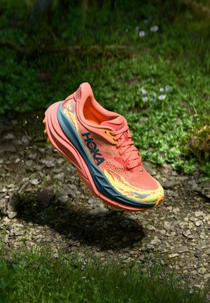 Hoka running shoe with a bright orange upper, blue-gray midsole, and yellow accents. Features textured surface and distinctive brand logo.