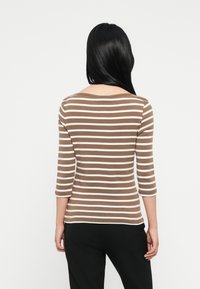 Ριγέ καφέ και λευκό τοπ με μακριά μανίκια και στρογγυλή λαιμόκοψη. Διαθέτει μανίκια τριών τεταρτημορίων και ευθύ στρίφωμα, φορεμένο με μαύρο παντελόνι.