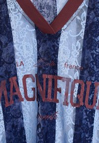 Spitzenstoff-T-Shirt mit blauen und weißen Streifen, bordeauxrotem V-Ausschnitt und auffälligem roten Text, der "MAGNIFIQUE" und "LA Belle France" liest.