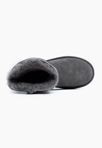Zapatilla de ante gris con un suave y esponjoso forro gris y una suela negra plana, que presenta una abertura redonda y un acabado de costura neat en los bordes.