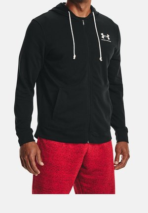 Mand iført sort lynlåstrøje med hvide snore og Under Armour-logo, kombineret med røde sportsshorts.