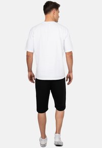 T-shirt blanc à manches courtes et shorts noirs à longueur de genou. Le T-shirt a un col rond ; les shorts ont une taille élastique et sont unis.
