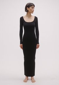 Juoda ilgos rankovės, prie kūno prigludusi suknelė su kvadratine iškirpte; pagaminta iš lygaus audinio, grindų ilgio, minimalistinio dizaino.