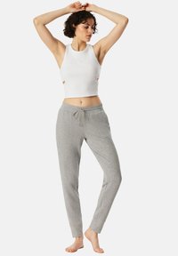 Bílý crop top s výřezy, doplněný o světlé šedé joggingové kalhoty s elastickým pasem a stahovací šňůrkou. Měkká, casual látka.
