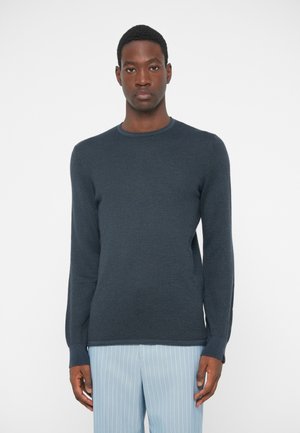 Pull en maille texturée bleu foncé avec des manches longues et un col rond. Associé à un pantalon rayé bleu clair.