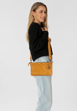 Borsa a tracolla gialla in pelle con tracolla regolabile, caratterizzata da un emblema a forma di ancora circolare, superficie liscia e chiusura a zip.