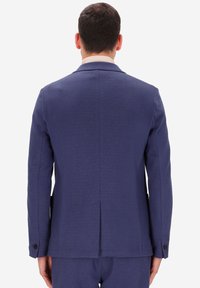 Blazer blu navy con un design aderente, caratterizzato da uno spacco posteriore e polsini con bottoni. Realizzato in un tessuto testurizzato per un aspetto strutturato.
