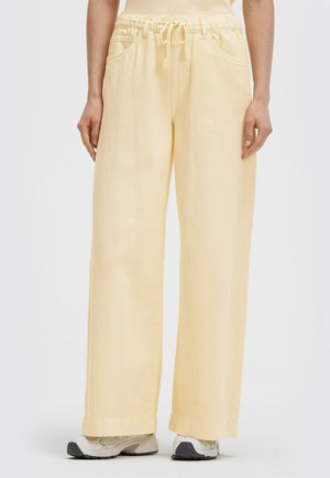 Wide-leg light yellow pants with elastic drawstring waist worn with white sneakers on a standing person.