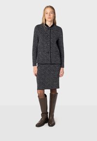 Cardigan grigio lavorato a maglia con colletto tondo, bottoni neri e gonna coordinata fino al ginocchio. Indossato con stivali alti in pelle marrone.
