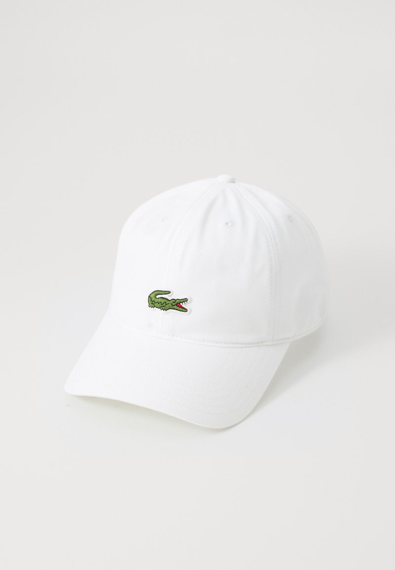 Hvit baseballcap laget av stoff med en grønn brodert krokodillelogo på fronten og en buet skjerm.