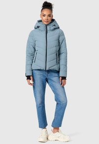 Gevoerde lichtblauwe jas met een ritssluiting aan de voorkant, hoge kraag, verstelbare capuchon en zwarte ritszakken aan de zijkant. Draag met blauwe jeans en sneakers.