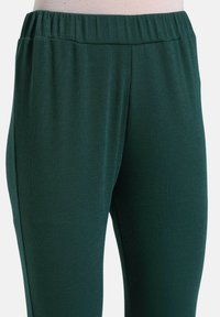 Dark green ribbed knit leggings with an elastic waistband, featuring a smooth texture and tailored fit. No visible seams or pockets.