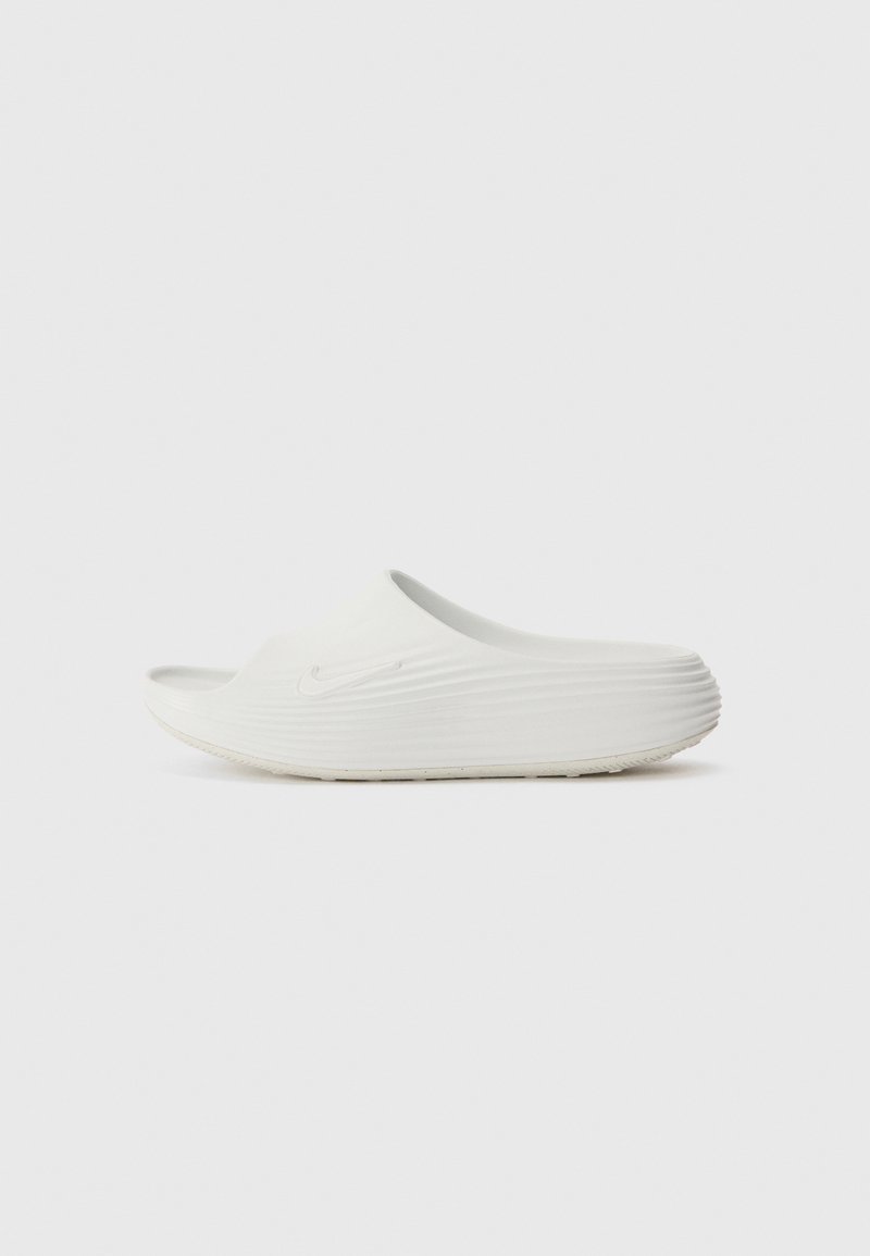 White clog with a ridged design, smooth texture, and rounded toe. Features a subtle logo and a flat sole with minimal detailing.