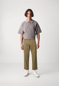 Grå kortærmet polo med krave, tekstureret stof og tre knapper, parret med grønne bukser og hvide sneakers.