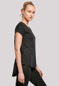 Camiseta negra de manga corta con escote en V y aberturas en los laterales. Hecha de un tejido suave, diseñada para un ajuste relajado. Con detalle azul en la manga.
