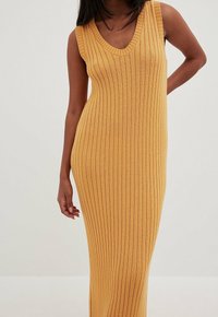 Robe sans manches en maille côtelée jaune moutarde avec un décolleté en V ; présente des rayures verticales et une silhouette ajustée, mettant en valeur la texture.