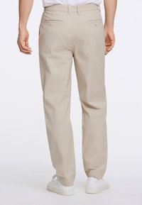 Beige byxor i lätt material med avslappnad passform, med två bakfickor och en slät textur. Bärs med vita sneakers.