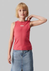 Top sin mangas rojo con textura acanalada y cuello redondo, combinado con una falda de mezclilla azul clara que presenta una abertura frontal.