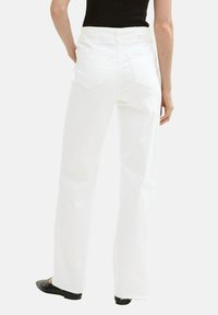 Pantalones de mezclilla blancos de pierna ancha con dobladillo sin acabar, dos bolsillos traseros y cintura alta. Combinados con una blusa negra y zapatos planos negros.