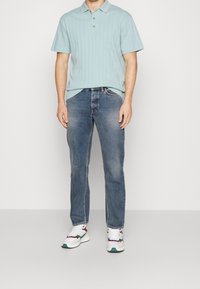 Polo shirt azzurro chiaro a maniche corte con un design a strisce testurizzate, abbinato a jeans blu scuro e sneaker bianche con accenti colorati.