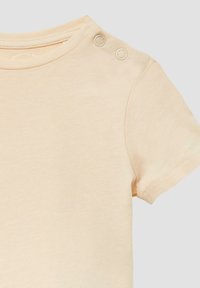 Lichtbeige t-shirt met korte mouwen, gemaakt van zachte katoen, met twee decoratieve knopen op de schouder en een ronde halslijn.