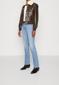 Giacca bomber in pelle marrone con colletto in finta pelliccia, due tasche sul petto, abbinata a jeans a gamba dritta di colore blu chiaro e stivaletti neri.