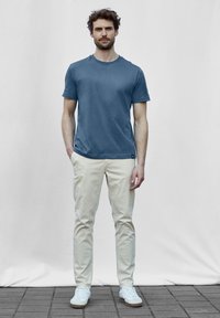 Modré tričko s krátkým rukávem vyrobené z měkké látky, doplněné krémovými chinos kalhotami a bílými teniskami. Jednoduchý design, bez viditelných vzorů.