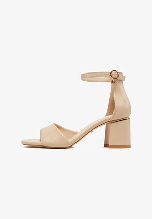 Beżowy sandał na słupku z odkrytymi palcami, paskiem na kostkę i złotym detalem klamry.
