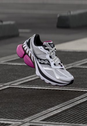 White athletic shoe featuring a mesh upper with black accents and pink details; thick outsole with a unique, contoured design.