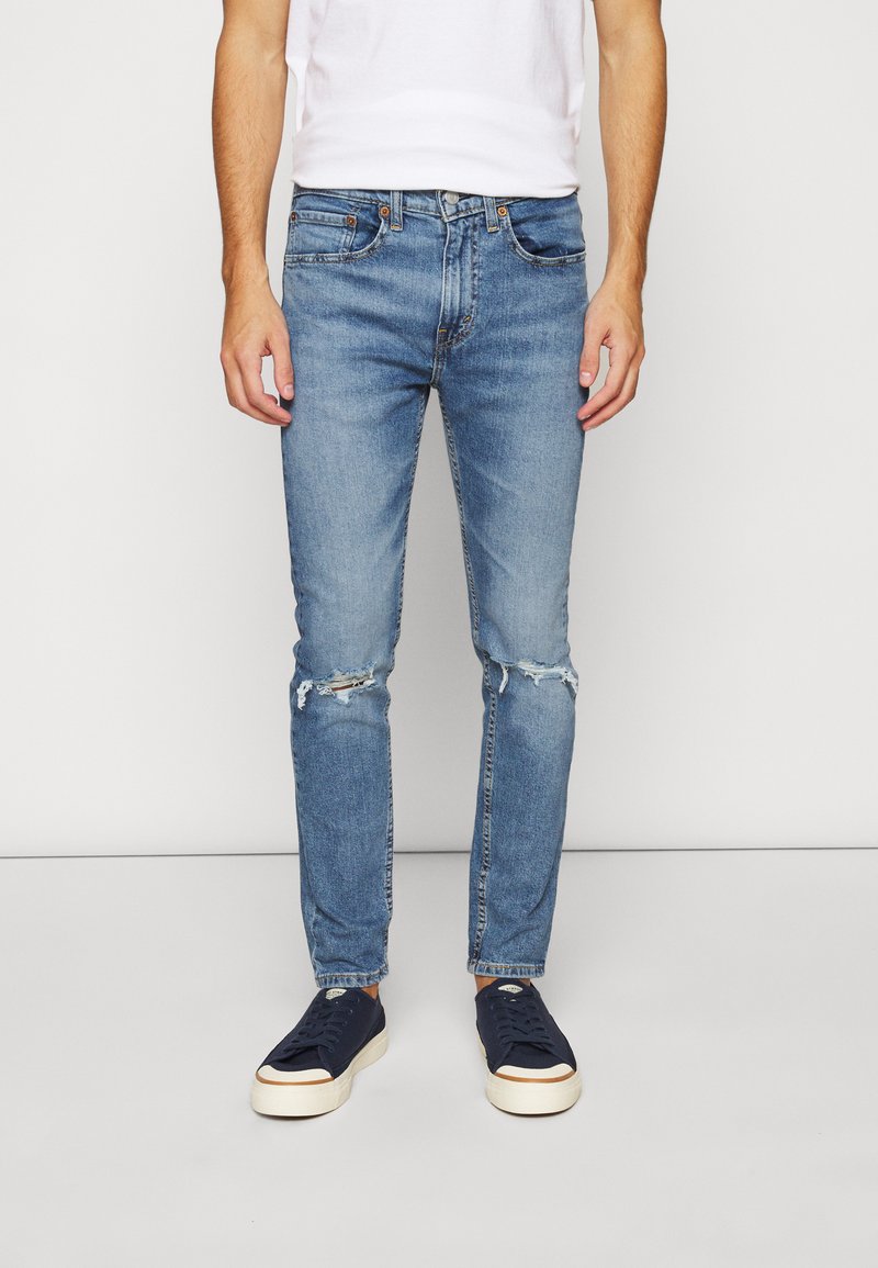 Helle blaue, verwaschene Jeans im Slim-Fit mit Rissen an den Knien und einem klassischen Fünf-Taschen-Design, kombiniert mit dunklen Sneakers.