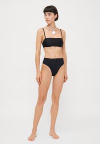 Schwarzes Zweiteiler-Bikini mit einem Bandeau-Top und dünnen Trägern sowie hochgeschnittenen Slips. Glattes Material, minimalistisches Design, ohne Muster.