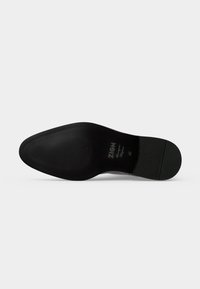 Semelle de chaussure noire à bout pointu, embossée avec "ZIGN Handmade," et marquage taille 42 sur un fond clair uni.