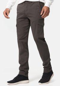 Pantalones cargo gris oscuro con bolsillos laterales, un diseño ajustado y material de mezcla de algodón. Combinados con zapatillas negras.