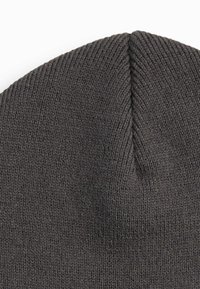 Gray knitted beanie with a tapered crown. Made of soft, textured material, featuring fine ribbing and a seamless top.
