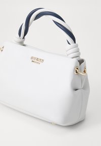 Sac à main en simili cuir blanc avec un design plié, une poignée torsadée bleu et blanc, des ferrures dorées et un logo en métal à l'avant.