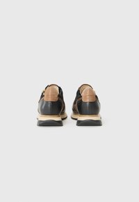Schwarze und braune Schuhe mit einem glatten Lederobermaterial, Wildlederelementen und einer beigen Zwischensohle. Strukturiertes Gummisohle und Reißverschlussdetail auf der Rückseite.