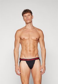 Schwarzer Herren-Thong mit rotem HUGO-Bund. Aus weichem Stoff gefertigt, bietet er eine enganliegende Passform und minimalen Anteil an Bedeckung. Klassisches Design ohne Muster.