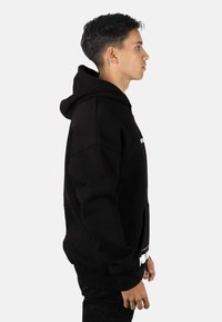 Sudadera con capucha negra con bolsillo tipo canguro, puños y dobladillo acanalados. Presenta un logo de texto blanco en el frente, hecha de una tela suave.