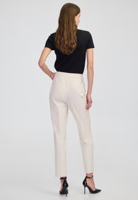 Beige op maat gemaakte broeken met een elastische taille, recht gesneden ontwerp, gladde textuur, gecombineerd met een aansluitend zwart T-shirt met korte mouwen en zwarte hoge hakken.