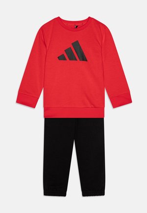 Sudadera roja con el logo de adidas en negro, combinada con pantalones negros con puños elásticos. Tejido suave con un diseño sencillo y deportivo.
