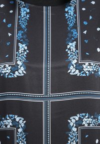 Black fabric top with intricate blue floral pattern, bordered by white accents. Features a round neckline and smooth texture.