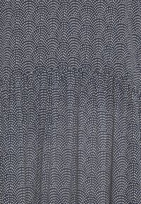 Marinfärgad tyg med ett mönster av vita prickar, med enresår vid midjan. Texturen ser slät och lätt ut.